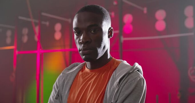 African American man standing arms crossed, camera moving closer, posing for promo in orange shirt