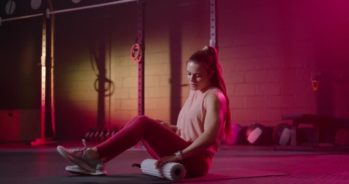 Female in leggings spotting, grabbing roller, rolling right calf on gym mat for release, copy space