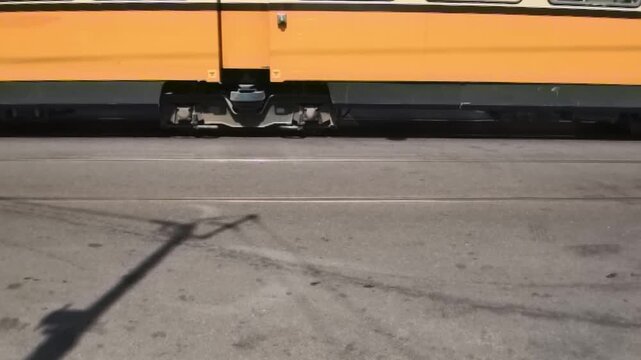 Horizontal 1080p 240fps ultra slow motion low angle video of city tram bogie wheels moving on steel tracks with sharp street shadow in the foreground asphalt