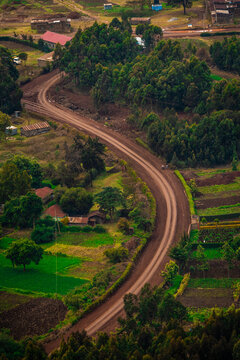 Aerial view of a winding dirt road cutting through lush green fields, scattered trees, and small rural houses in Nairobi, Nairobi County, Kenya.