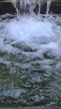 Vertical cinematic 1080p 240fps ultra slow motion video of fountain water falling close up. Widescreen anamorphic lens aspect ratio look, splashing liquid stream with white foam background texture