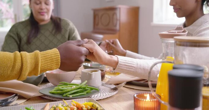 African American family reaching, holding hands at dining table before meal with candle, carafe