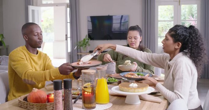 African American friends serving at dining table man extending plate, center ladling, right tonging