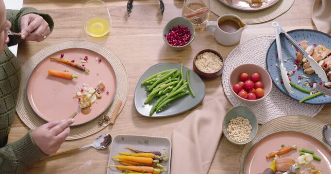 Family starting meal, African-American woman green sweater serving protein with tongs at home table