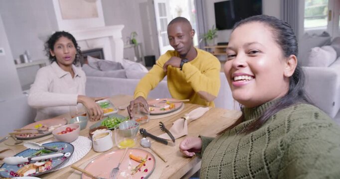 African American friends recording selfie on phone after meal at home table passing veggies, waving