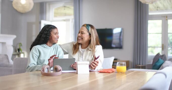 African American mother and preteen daughter tapping tablet, mother wrapping arm, sharing content
