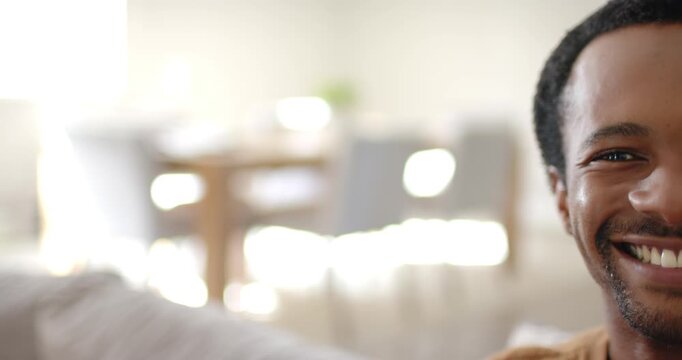 Man smiling into camera after prompt, wearing brown top in living room, potted plant, copy space
