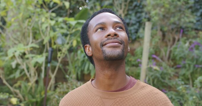 African man wearing quilted top noticing movement above turning head and smiling in garden