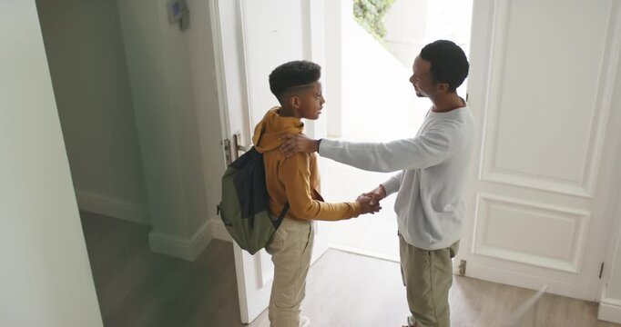 African American dad teen son front door open patting shoulder, handshake son leaving with backpack