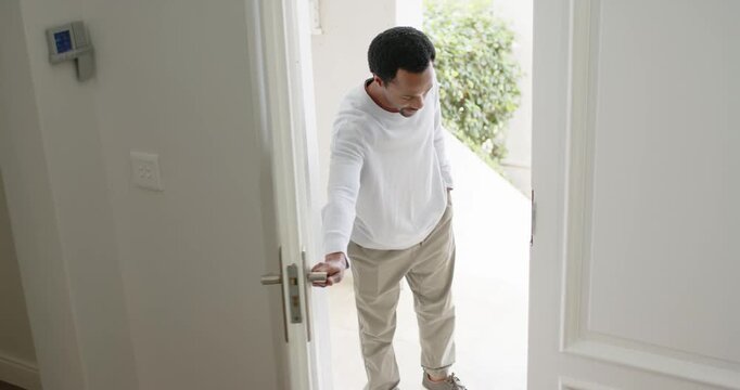 African American dad noticing teen on porch, opening double doors, welcoming son with backpack in