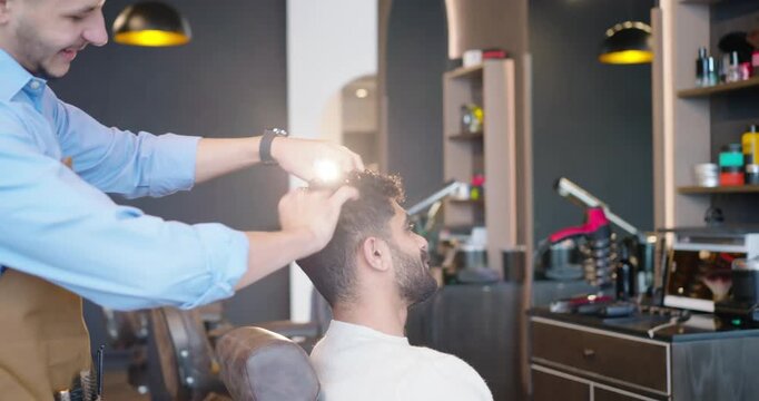 African American male barber and male client on request, shaping curls with comb, clippers at shop