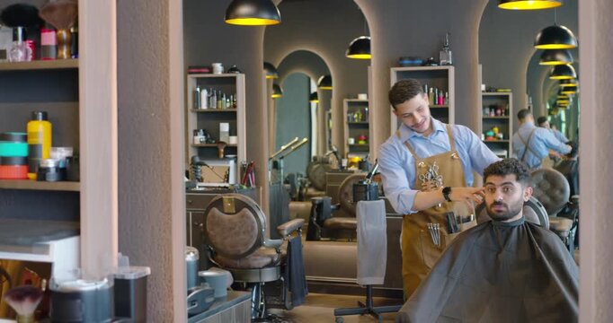 African American barber adjusting cape and steadying client jaw, combing, trimming hair at mirror