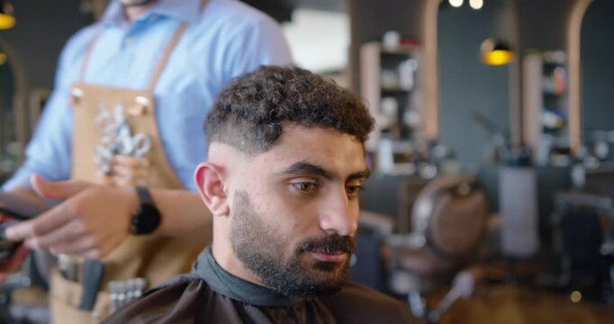 Barber trimming African American man sitting, creating skin-fade using clippers in barbershop