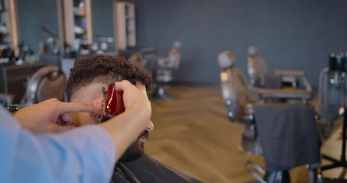 Barber starting nape clipping male client at shop using red trimmer shaping taper fade, copy space