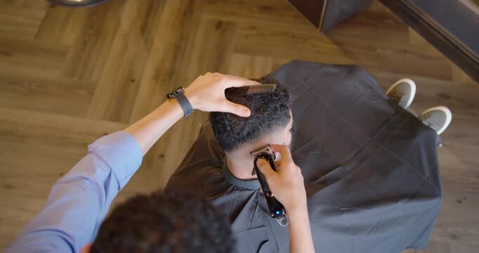 Two African American men, barber placing cordless clipper at nape using comb, shaping fade in shop