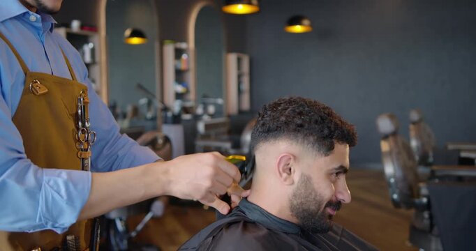 African American barber and client at shop, barber placing hand on head, trimming fade with clipper