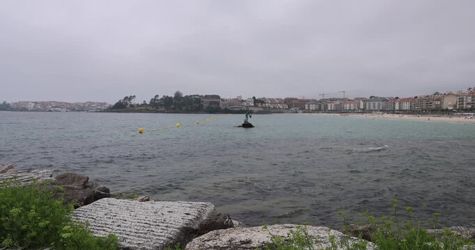 Bronze sculpture of madama de silgar standing on rocks in the water near the beach