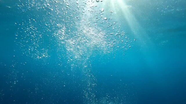 Underwater view of sunlight filtering through clear blue water with a stream of bubbles rising towards the surface