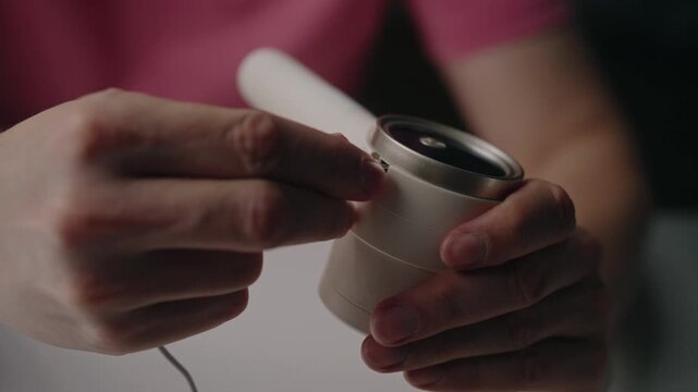 Close-up of hands connecting white charging cable to portable electric lint remover machine at table, modern household appliance for clothing care and fabric maintenance. Shooting in slow motion.