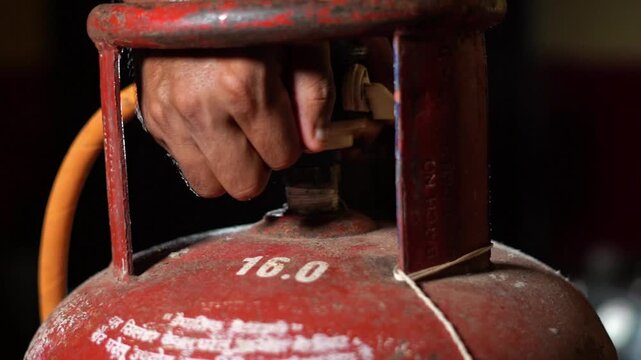 Indian Man Hand Turning Off Valve on Red LPG Gas Cylinder Close Up. Close Up of Indian Householder Ensuring Safety on Domestic LPG Tank. Red LPG Cylinder in India.