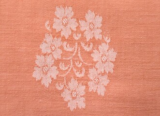 Background view of an elegant peach jacquard fabric, featuring a delicately woven floral motif at its center. © Antonios