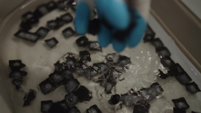 Close-up of technician gloved hand cleaning and disinfecting mechanical keyboard keys in basin of water, ensuring thorough sanitation process for computer peripherals. Shooting in slow motion