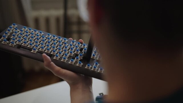 Closeup view from over shoulder of it specialist, hobbyist cleaning blue switches of custom mechanical keyboard with special brush, performing routine maintenance. Shooting in slow motion