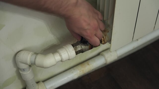 Close-up of a hand opening and closing a valve on a radiator