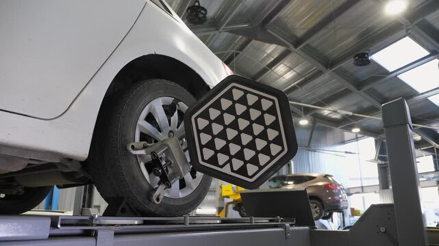 Diagnostics and balancing of wheels on a lift at a close-up view at a modern service station. The car moves slowly with wheel balancing equipment.