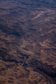Aerial view of a winding river cutting through the arid, rugged landscape of the Great Rift Valley with dry terrain and deep canyons in Nairobi, Nairobi County, Kenya.