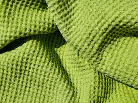 Background view of a crumpled lime green waffle fabric texture, full frame honeycomb weave textile pattern.