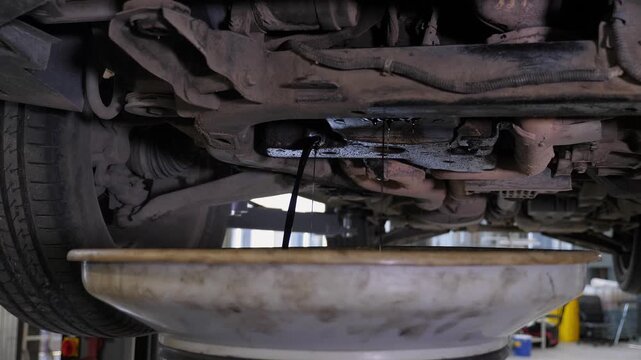 A detailed view of the underside of the vehicle after an oil change, with a stream of water at the service station. The technician is cleaning the underside of the car using a specialized device.