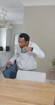Vertical video: African American dad entering as teen son packing lunch for school, dad sipping mug