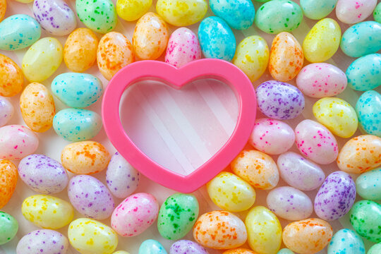 Colorful Speckled Jelly Beans Surrounding a Pink Heart on a Pink Striped Background