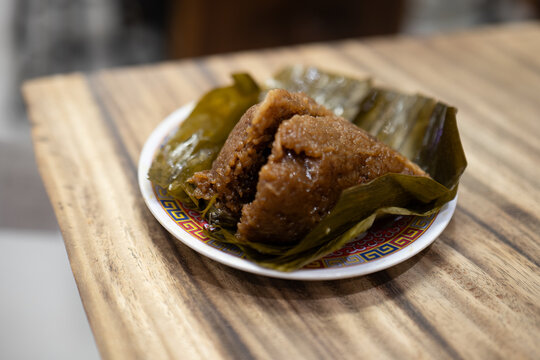 A close-up shot of a savory Chinese Zongzi (also known as Bacang or Bakcang), a pyramid-shaped sticky glutinous rice dumpling unwrapped from its bamboo or banana leaf casing, served on a small pattern