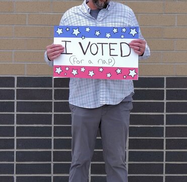 Man holding a humorous, satirical campaign sign reading I Voted for a nap, capturing themes of election fatigue, voting fatigue, and political burnout