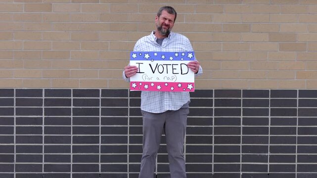 Man holding a humorous, satirical campaign sign reading I Voted for a nap, capturing themes of election fatigue, voting fatigue, and political burnout