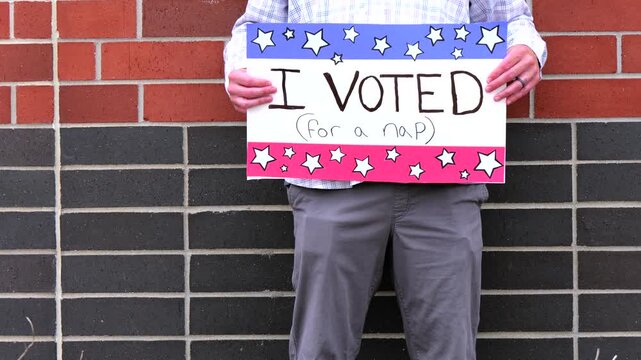 Man holding a humorous, satirical campaign sign reading I Voted for a nap, capturing themes of election fatigue, voting fatigue, and political burnout