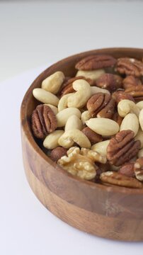 Wooden bowl filled with variety of nuts including almonds, hazelnuts, pecans, walnuts and cashews. Close-up highlights fresh ingredients, rich texture and naturally nourishing food for balanced eating