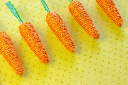 Yarn Woven Orange Carrots in a Row on a Yellow Spotted Background
