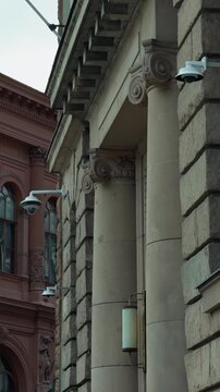 Historic urban building facades with classical columns, carved stone details, dome security cameras, and muted daylight creating strong architectural texture and vertical perspective