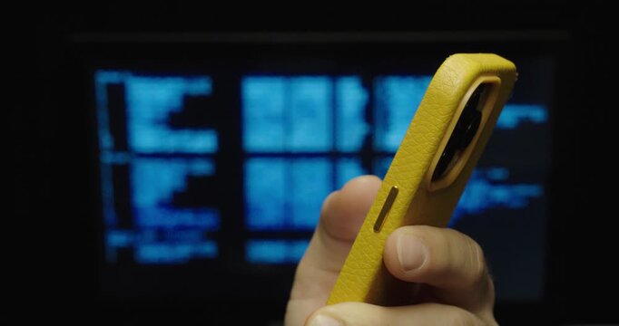 Close-up of a smartphone held in hand with a blurred computer code screen in the background.