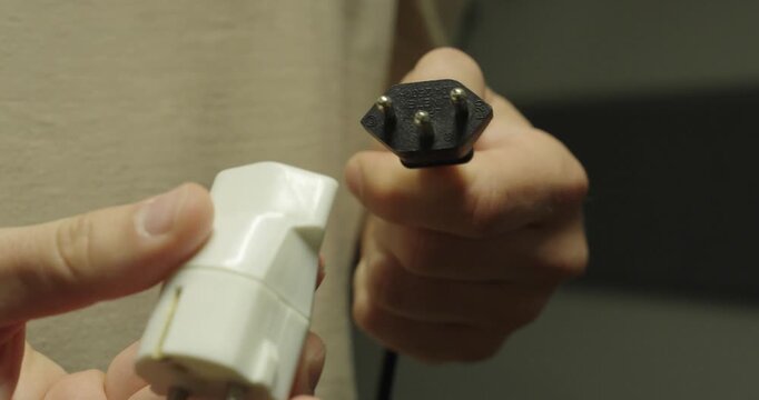 Close-up of hands connecting an international travel power adapter to an electrical plug. Useful concept for travel preparation, electricity compatibility, and global power connections.
