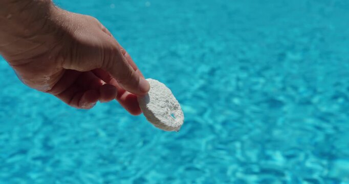 Close-up of a chlorine tablet held above a swimming pool before use. Pool maintenance, water disinfection, hygiene, and swimming pool care concept.