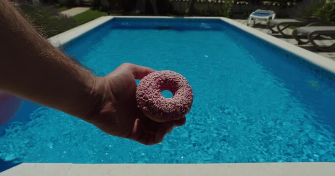 Donut held beside a swimming pool to illustrate pool rules prohibiting food consumption in or near the water. Pool hygiene, cleanliness, safety, and facility regulations concept.