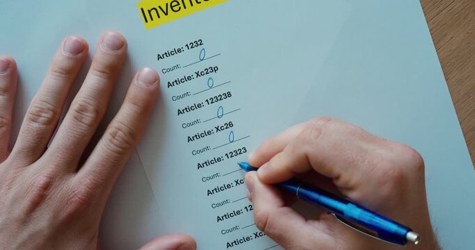 person writing inventory quantities on a printed stock checklist during a warehouse inventory count. Inventory management, stocktaking, logistics, and business administration concept.
