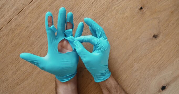 Top-down view of damaged disposable gloves with holes in the fingertips, demonstrating the need to replace torn gloves to maintain hygiene and personal protection. Workplace safety and PPE concept.