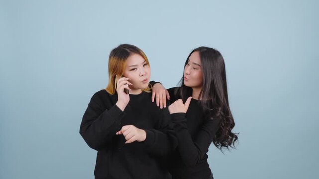 Two Asian women discussing news during a phone call on blue backdrop