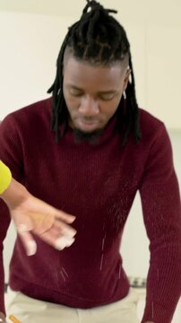 Vertical video: Reacting man in maroon kneading in kitchen as spouse in yellow adding flour cooking