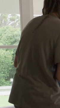 Vertical video: Opening door host in gray tee greeting friends entering doorway, holding sixpack